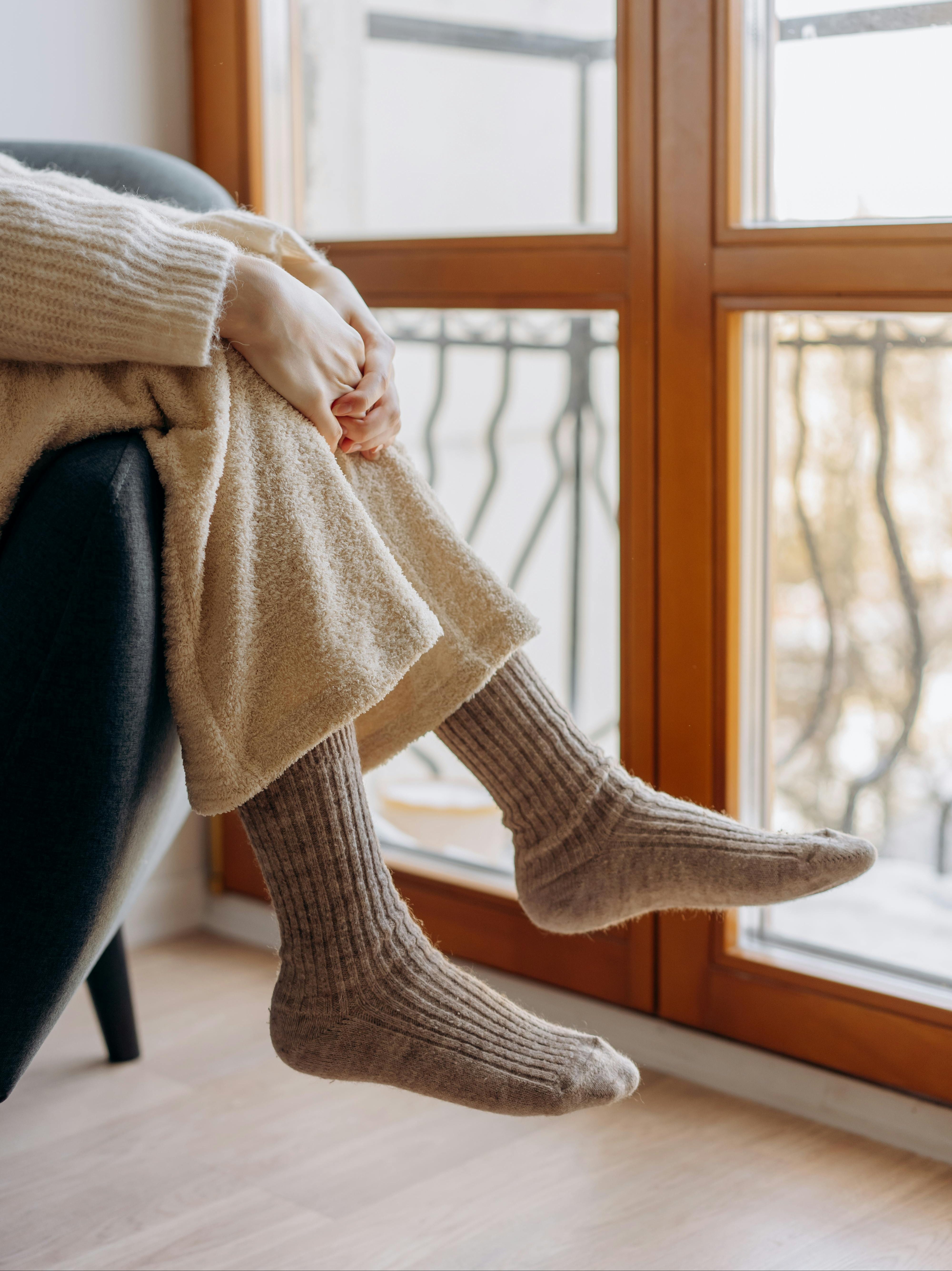 Frau sitzt mit Bademantel am Fenster. Sie trägt Wollsocken mit Alpakawolle an den Füßen.