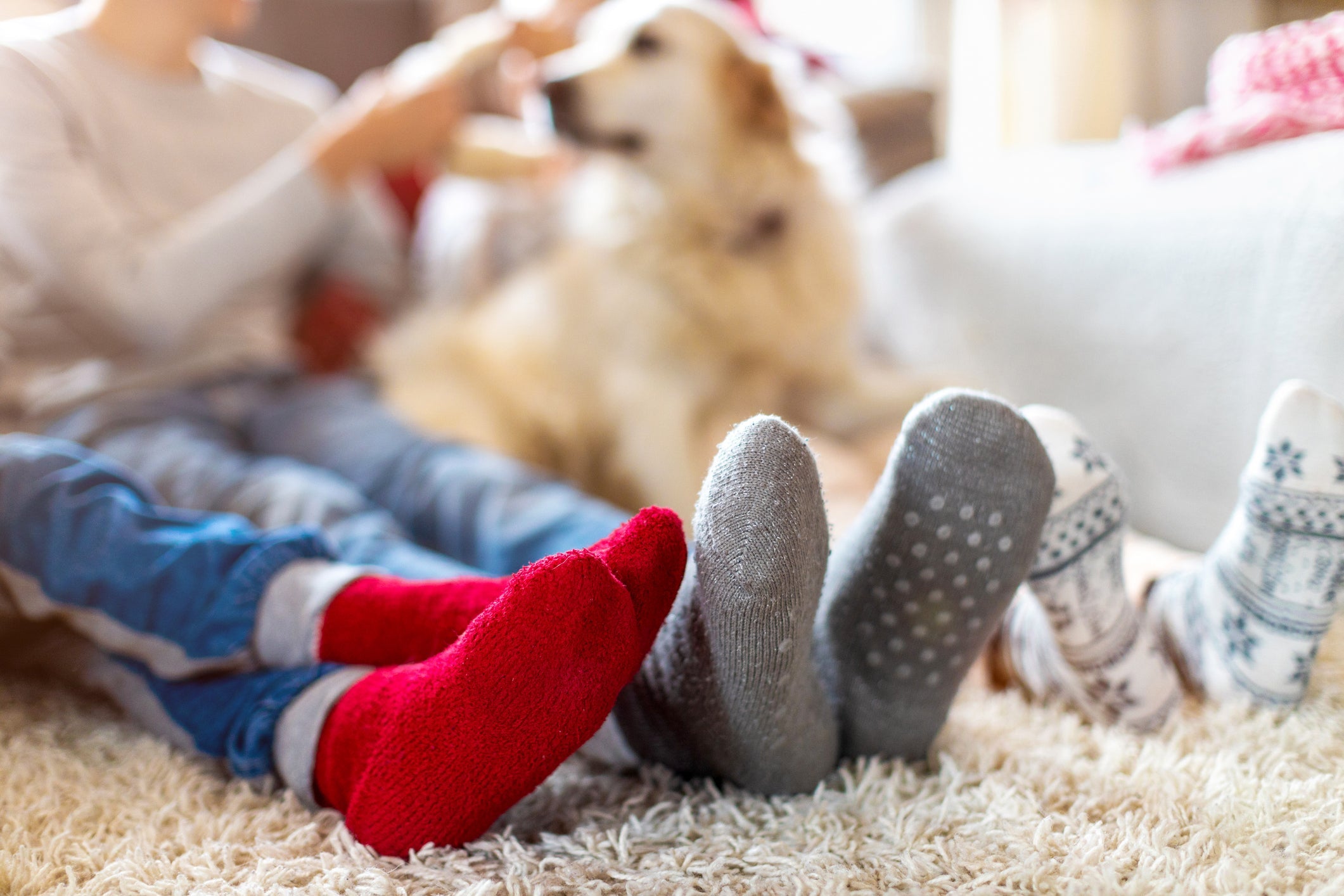 Nahaufnahme von drei Kindern, die gemütlich in warmen, farbigen Kindersocken auf einem Teppich liegen, mit einem Hund im Hintergrund